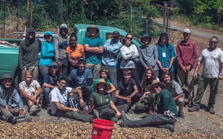A group of outward bound students stand in front of a green truck and pose for a photo during a service day